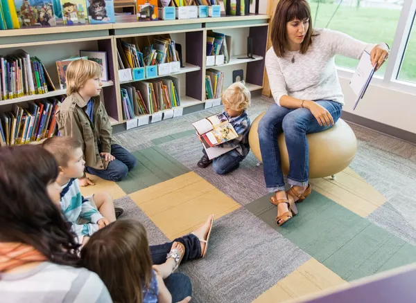 Teacher Reading Book To Children In Library