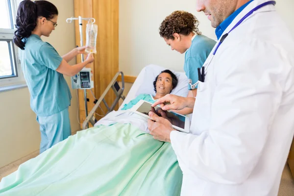 Doctor Using Digital Tablet With Nurses Examining Patient In Hos
