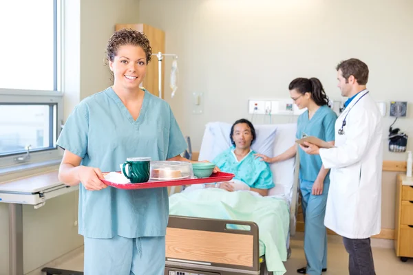 Nurse Holding Tray With Medical Team And Patient In Background