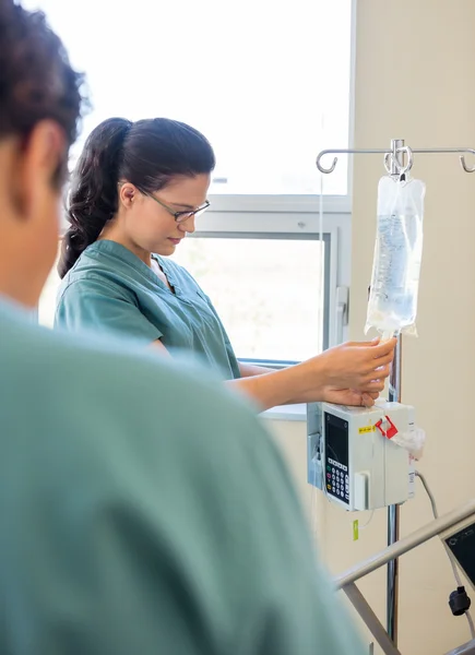 Nurse Adjusting IV Bag With Coworker In Foreground
