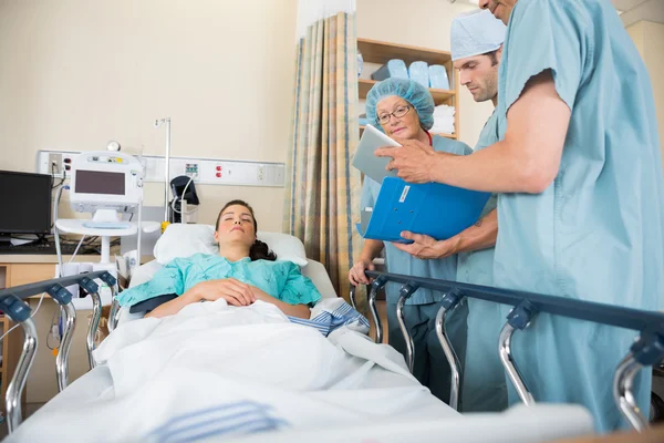 Nurses Discussing Patient's Report By Bed