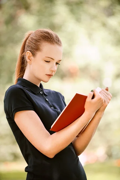 Young woman in dark blouse reads red book