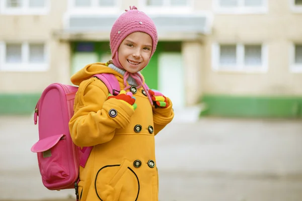 Smiling little girl in yellow coat with pink backpack