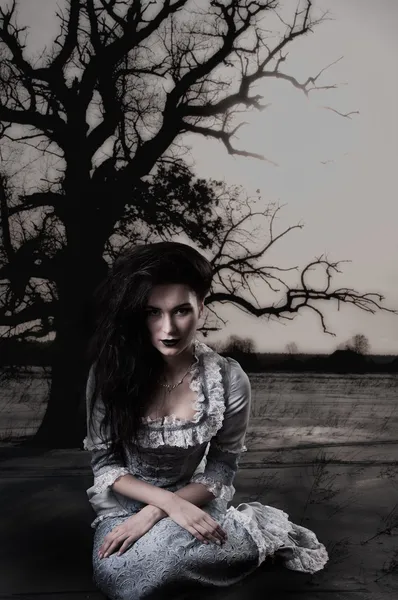 Weird female witch on background with dead tree