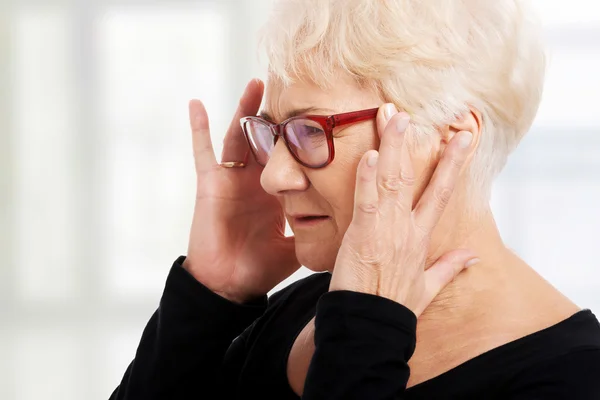 An old woman is eye glasses is having a headache.