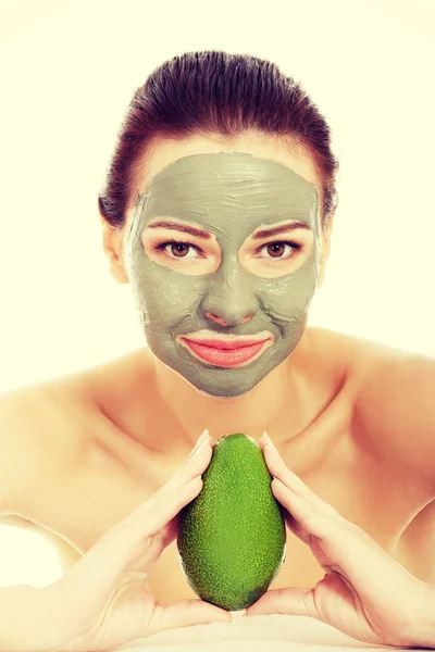 Beautiful woman with facial mask holding avocado