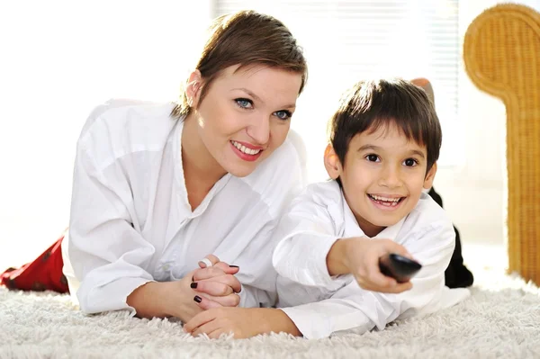 Mom with son lying on floor and watching tv using remote control