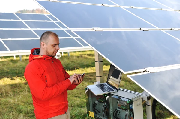 Engineer working with laptop by solar panels, talking on cell phone