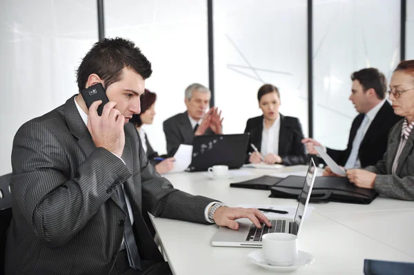 Business man speaking on the phone and typing on laptop while in a meeting