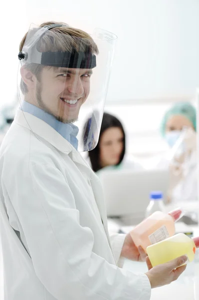 Young medical worker with glass mask working with his team in lab