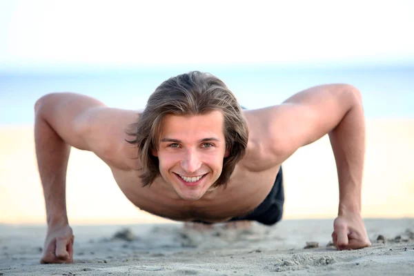Handsome man doing push ups on the beach