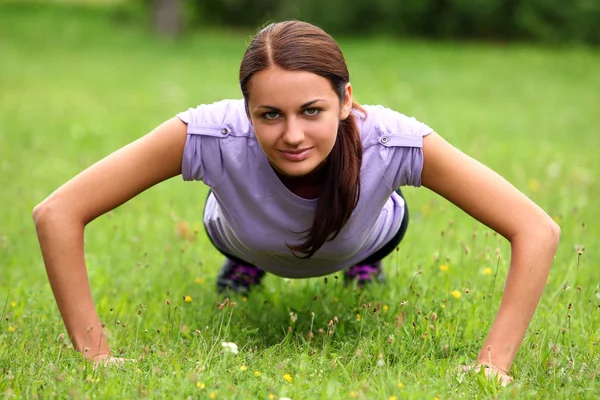 Young girl do her push-ups exercises in the park