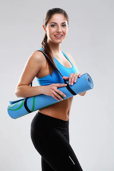 Young woman in fitness wear with mat