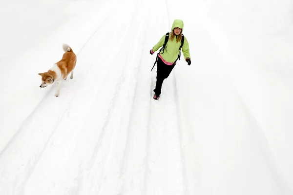 Woman hiking with dog on winter road and snow