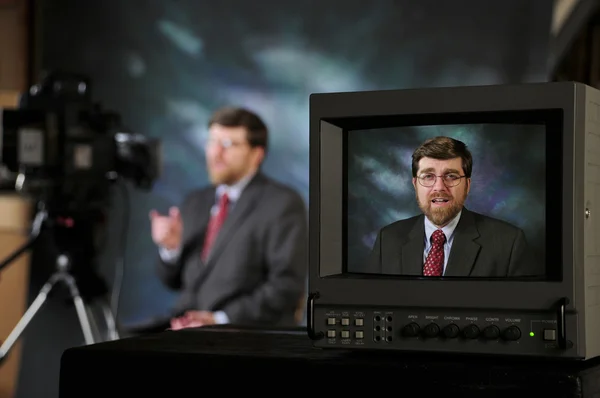 Monitor in TV production studio showing man talking to a camera