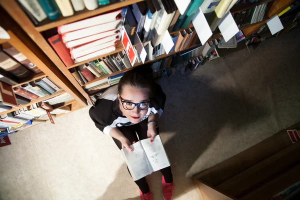 Young girl with glasses sitting in a rack with books