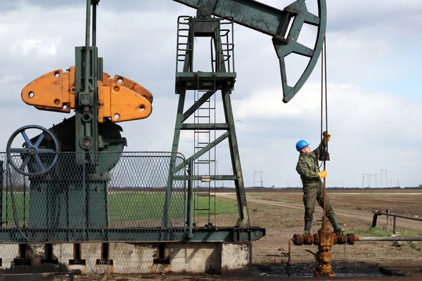 Oil worker standing at pipeline and check pump jack