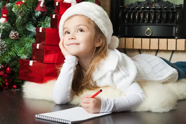 Pretty girl in Santa hat writes letter to Santa
