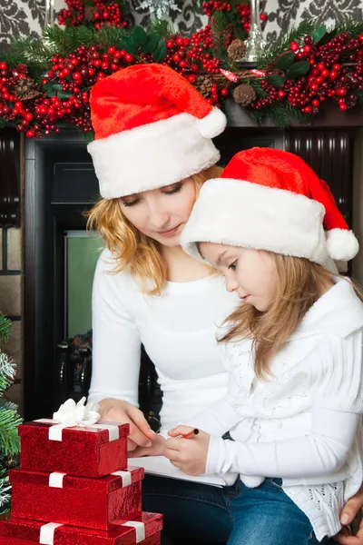 Girl and mother in Santa hats write letter to Santa