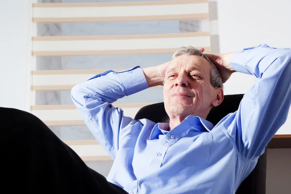 Senior businessman lying on his office chair with his feet on th