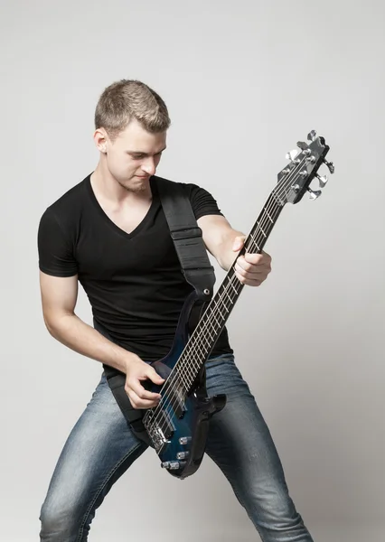 Young male musician playing a six-string bass guitar isolated on