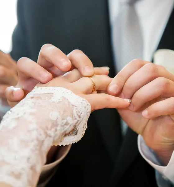 Mans hand putting a wedding ring on the brides finger