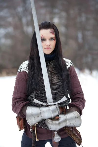 Beautiful young woman in medieval clothes holding a sword