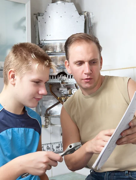 The father and the son-teenager together look the instruction on repair a gas water heate