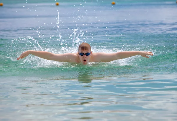 Young sporting man swims in the sea butterfly stroke style.