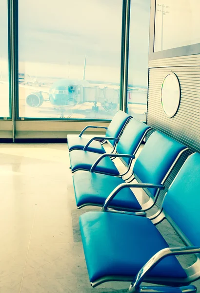 Empty armchairs in hall of expectation of airport and plane behind window,with a retro effect