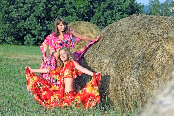 Two beautiful girls in bright clothes around haystacks