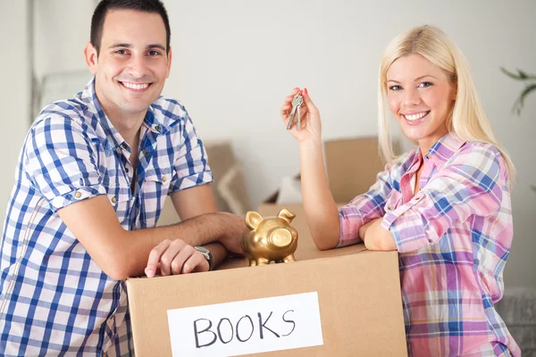 Couple with piggy bank and keys with moving boxes