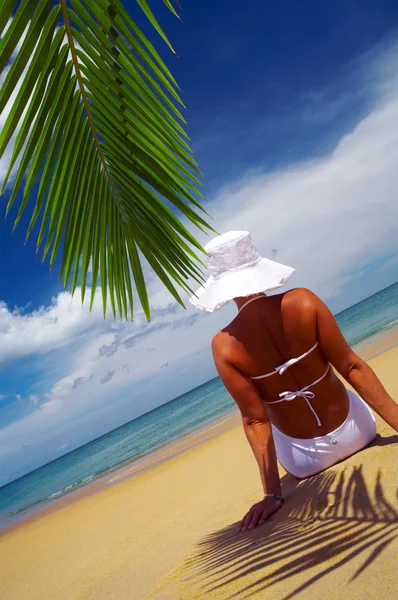 View of nice woman lounging on tropical beach in white panama and bikini