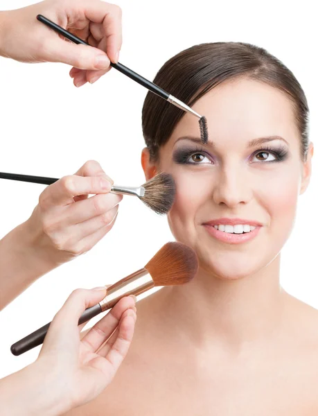 Three hands applying cosmetics on the woman's face with brushes