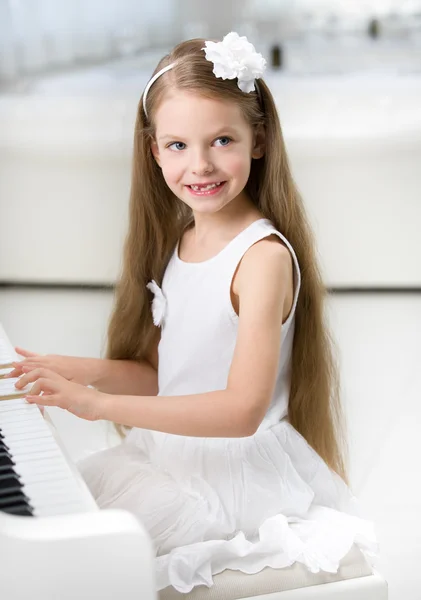 Portrait of little pianist in white dress playing piano