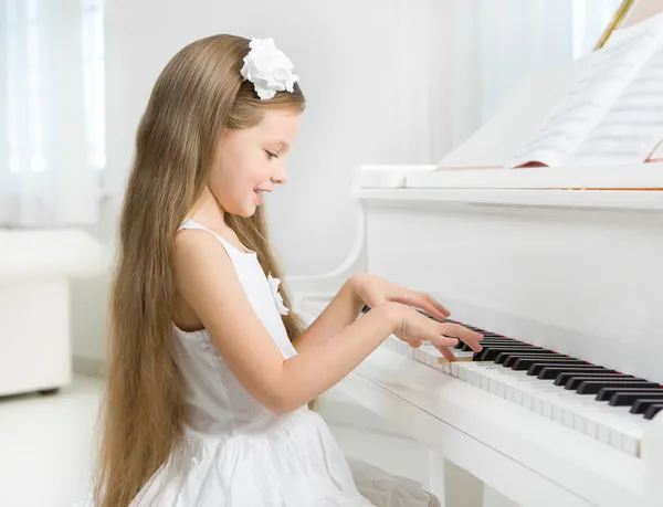 Profile of little girl in white dress playing piano