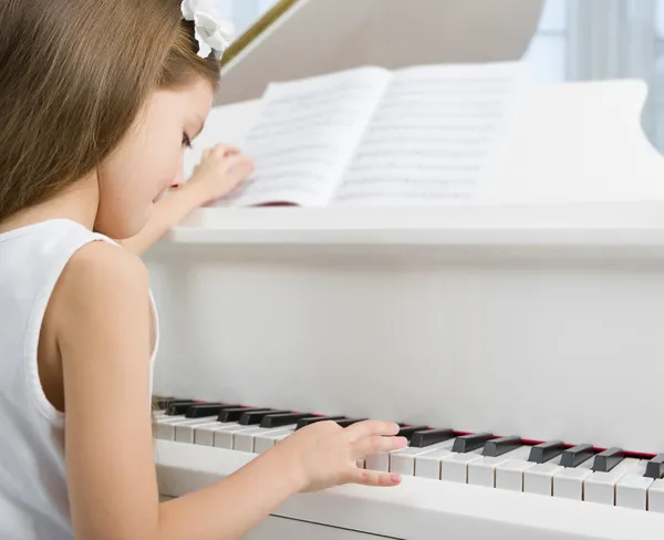 Side view of little child in white dress playing piano