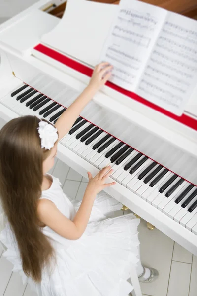 Top view of little girl in white dress playing piano