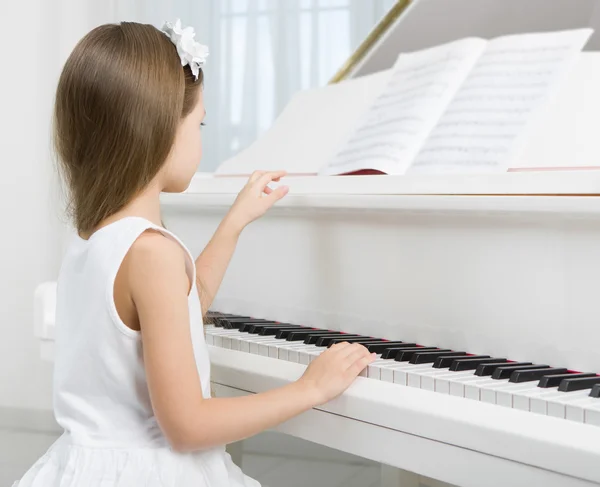 Side view of little girl in white dress playing piano