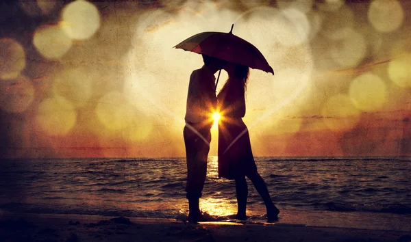 Couple kissing under umbrella at the beach in sunset. Photo in o