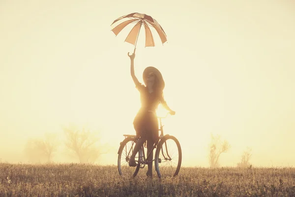 Girl with umbrella on a bike in the countryside in sunrise time