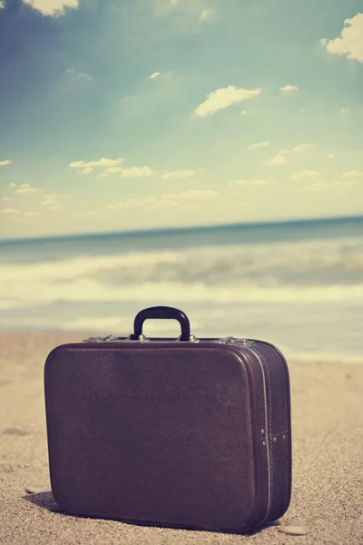 Retro travel suitcase is alone on a beach