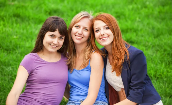 Redhead, brunette and blonde girl sitting at green grass in the