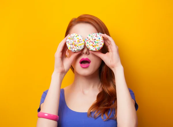 Redhead women with muffin on yellow background.