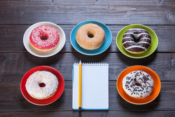 Notebook, donuts and pencil on wooden table.