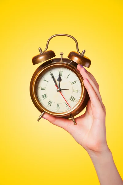 Hand holding alarm clock on yellow background.
