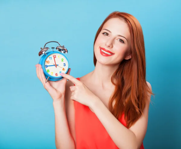 Smiling redhead women woth alarm clock on blue background.