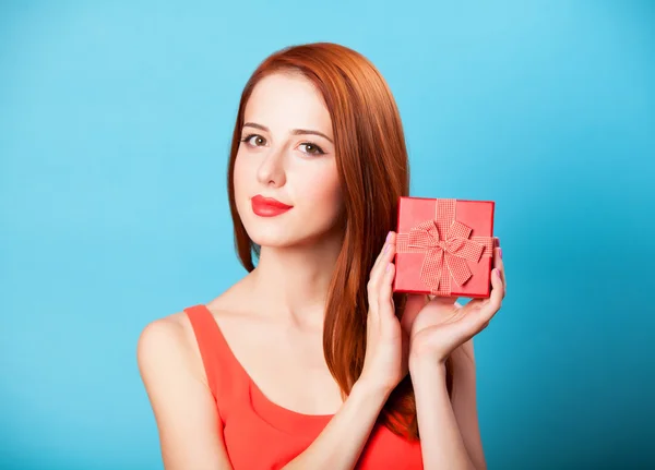 Smiling redhead women with gift on blue background.