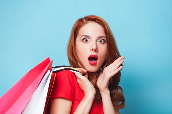 Surprised redhead girl with shopping bags on blue background.