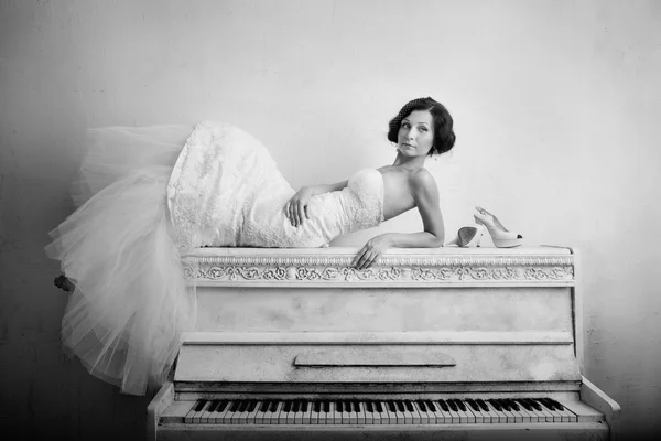 Beautiful woman in luxurious dress lying on the piano. Retro style — Stock Photo #24632429
